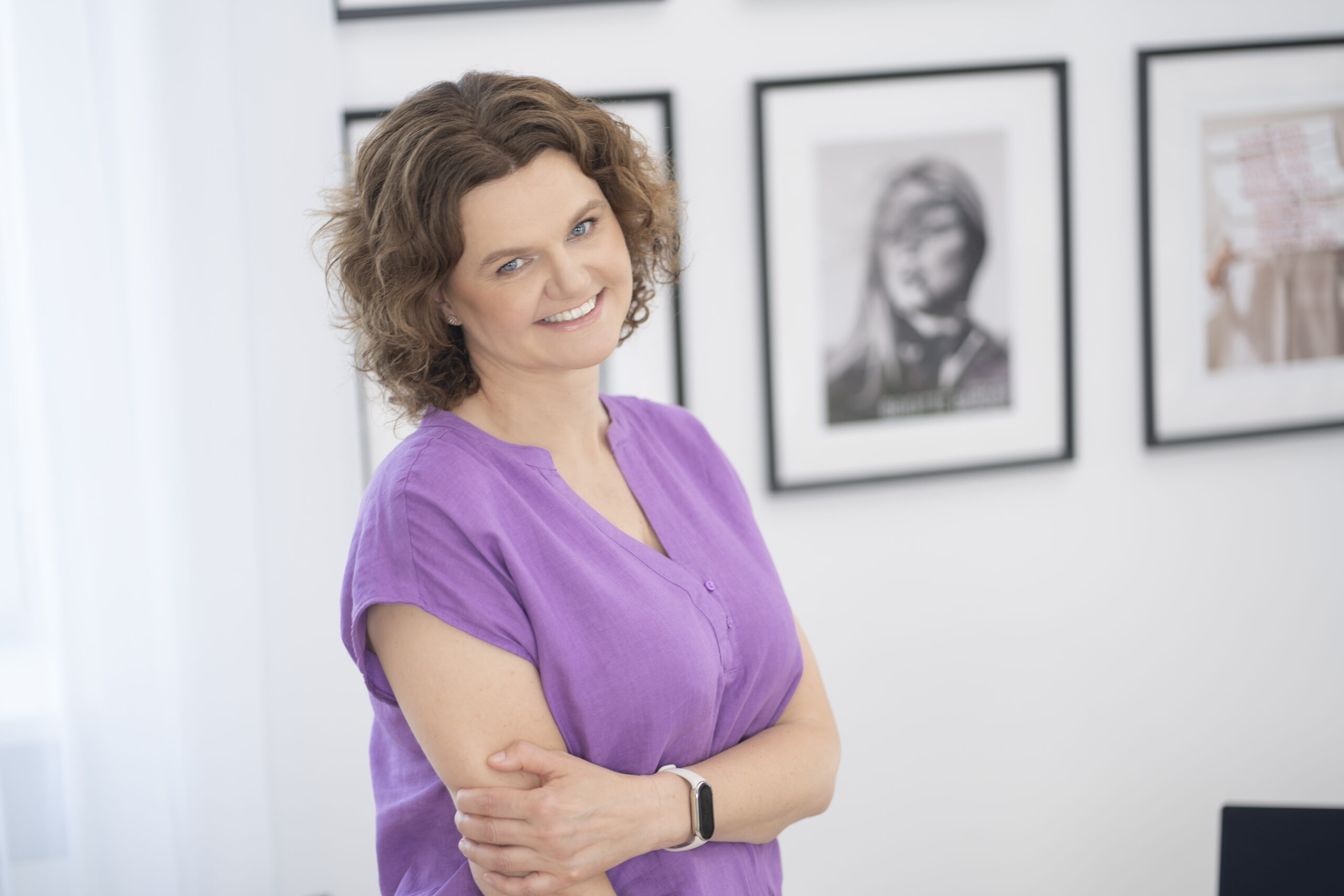 Joanna Gotfryd stoi z założonymi rękami w fioletowej bluzce